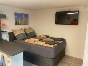 A compact room with a bed, a desk, a flat-screen TV, and a painting on the wall.