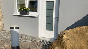 Ett hus med en vit dörr, ett fönster med en krukväxt och en entré som är belagd med sten.