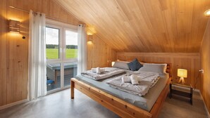 Un dormitorio con paneles de madera, una cama grande, una mesita de noche con lámpara y vistas a un campo verde a través de la ventana.