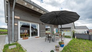 Un patio con una mesa y sillas, un paraguas grande y plantas en macetas.