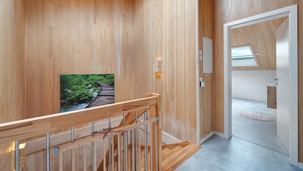 Un interior de madera con una escalera, un cuadro enmarcado y vistas a una habitación contigua.