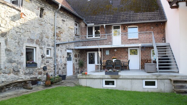 Ein zweistöckiges Haus mit Balkon, Treppe und kleinem Garten.