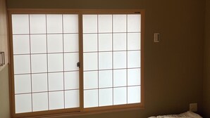 Une pièce dotée d’un sol recouvert de tatamis, d’un futon servant de lit, d’une porte coulissante de style shoji et d’un luminaire au plafond.