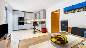 Eine moderne Küche mit weißen Schränken, ein Essbereich mit einem Holztisch und einer Obstschale.
