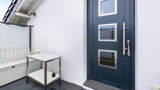 Eine dunkelblaue Tür mit drei rechteckigen Fenstern, einer weißen Bank und einem kleinen Tisch mit Metallgestell.
