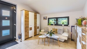 Ein modernes Wohnzimmer mit einer Couch, zwei kleinen Tischen, einem Fenster mit Blick ins Grüne und einem Schiebetürenschrank.