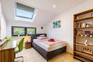 Ein Schlafzimmer mit einem Bett, einem Schreibtisch, einem Stuhl, einem Bücherregal und einem Oberlicht.