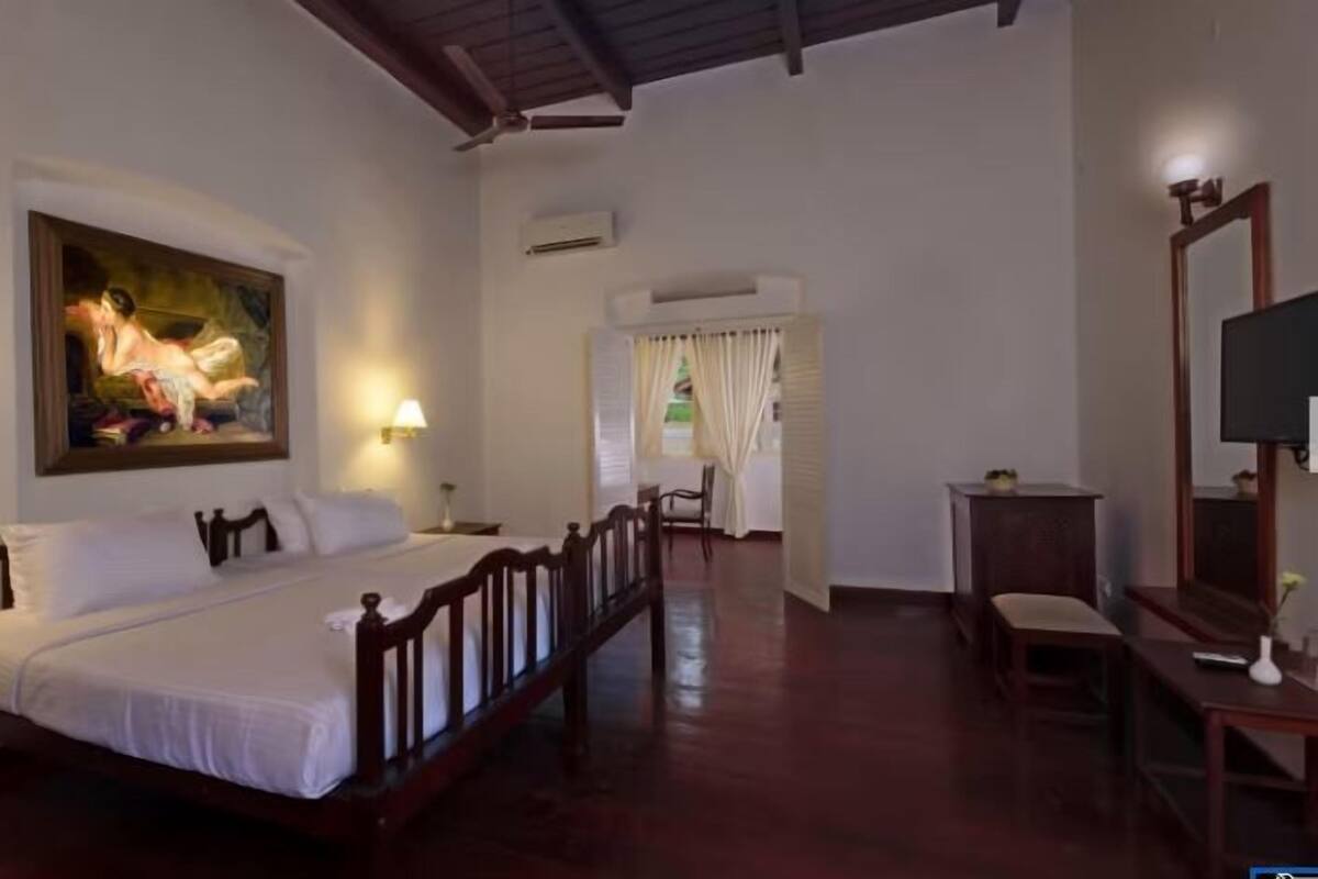 A bedroom with a wooden bed, a painting on the wall, a desk with a mirror, and a window with curtains.