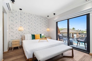 A bedroom with a large bed, a bench, a nightstand, a potted plant, and a view of a pool and outdoor seating area.