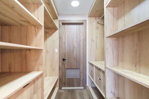 Un couloir étroit, avec des étagères en bois de part et d’autre, et une porte au fond.