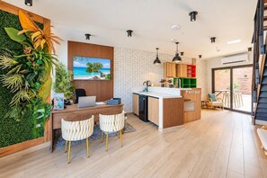 A modern kitchen with a wooden island, a dining area with two chairs, and a green wall with plants.