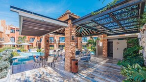 Un espace aménagé au bord de la piscine, comprenant un coin salon couvert, une piscine et un bâtiment à la façade en briques.