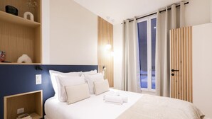 Ein ordentlich eingerichtetes Hotelzimmer mit einem großen Bett, Nachttischen, einer festen Ablage und Blick ins Freie durch eine Schiebetür.