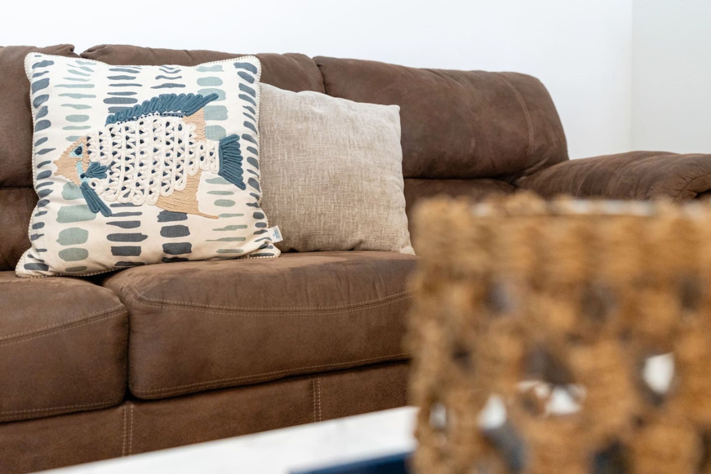 A brown sofa with two decorative pillows, one with a geometric pattern and the other plain.