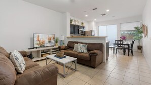 Un salon moderne avec un canapé en cuir marron, une table basse et un téléviseur. Il y a également un coin cuisine avec des placards et une table à manger avec des chaises.