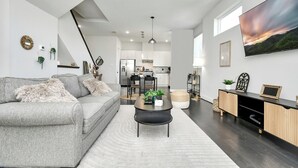 Un salon moderne avec un canapé gris, une table basse noire et un grand téléviseur fixé au mur.