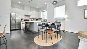Une cuisine moderne avec des meubles blancs, un réfrigérateur en acier inoxydable et un coin repas comprenant une table ronde et des chaises.