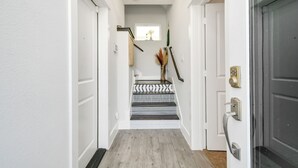 Un couloir avec un escalier, des murs blancs et un plancher en bois.