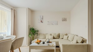 A living room with a sofa, a coffee table with fruits and a book, a dining area with chairs, and a potted plant. - Lumina apartments with 2 terrace (Warsaw)