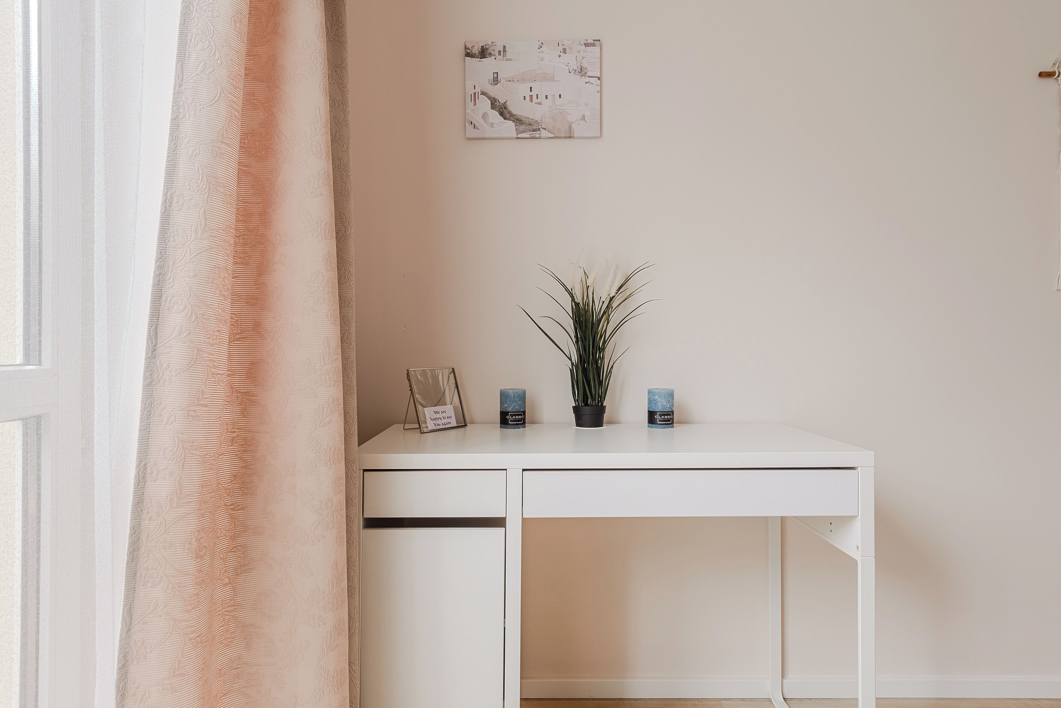 A white desk with a potted plant, two candles, and a framed picture on it.