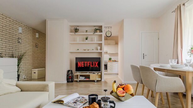 A modern living room with a flat-screen TV displaying "NETFLIX," a dining area with a wooden table, and a breakfast setup on a tray. - Lumina apartments with 2 terrace (Warsaw)