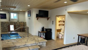 Quarto amplo com piscina de pedra, cama, televisão, micro-ondas e pequena cozinha.