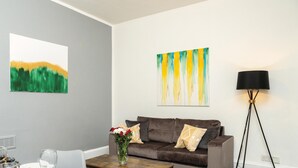 Een woonkamer met een grijze muur, een bruine bank, een bijzettafeltje, een vaas met bloemen en een vloerlamp.