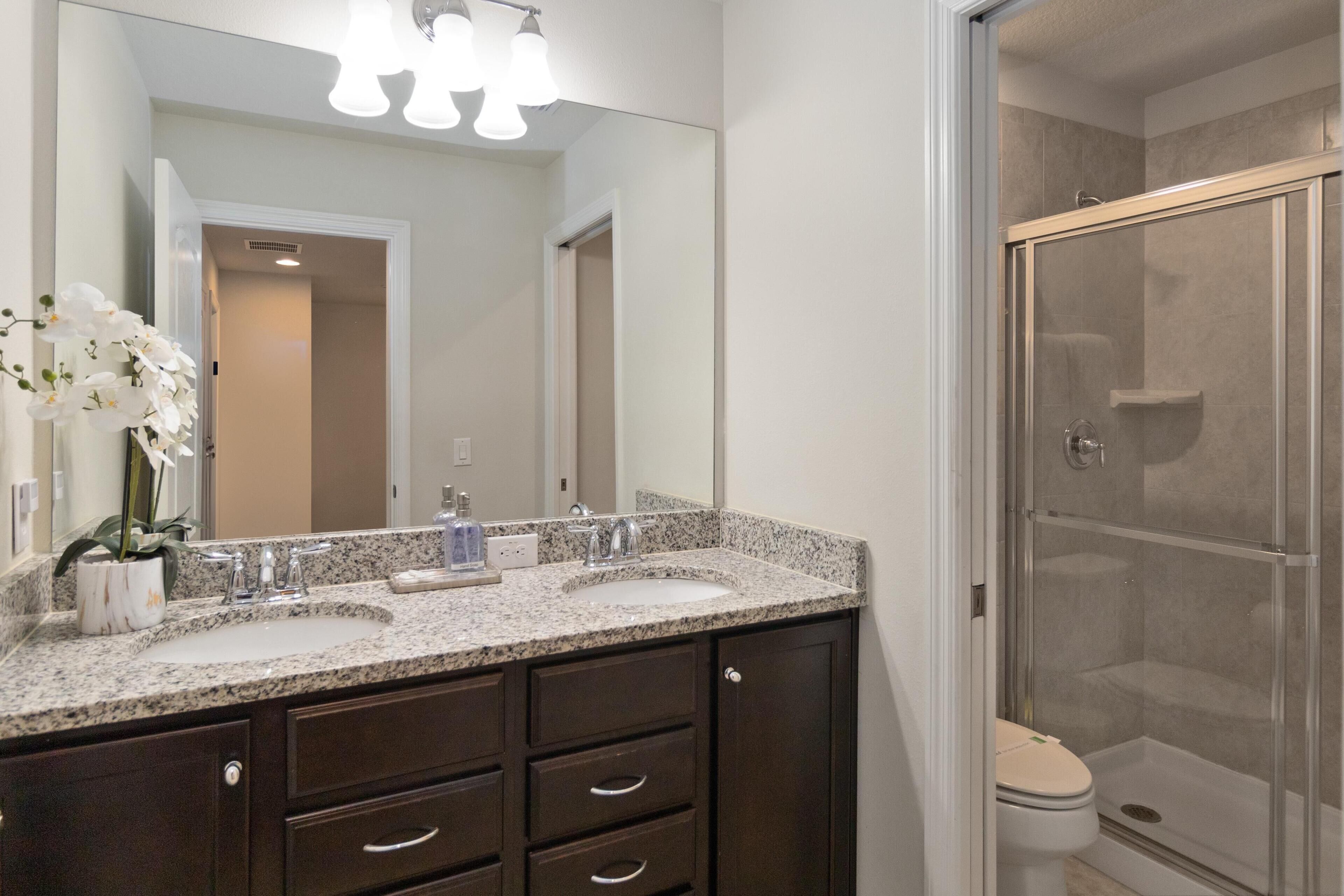 A bathroom with two sinks, a large mirror, and a glass-enclosed shower.