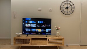 Un téléviseur à écran plat fixé au mur, une horloge et une console en bois sur laquelle est posé un vase de fleurs.