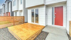 Un immeuble résidentiel moderne doté d’une terrasse en bois, d’une porte rouge et offrant une vue sur la propriété voisine.