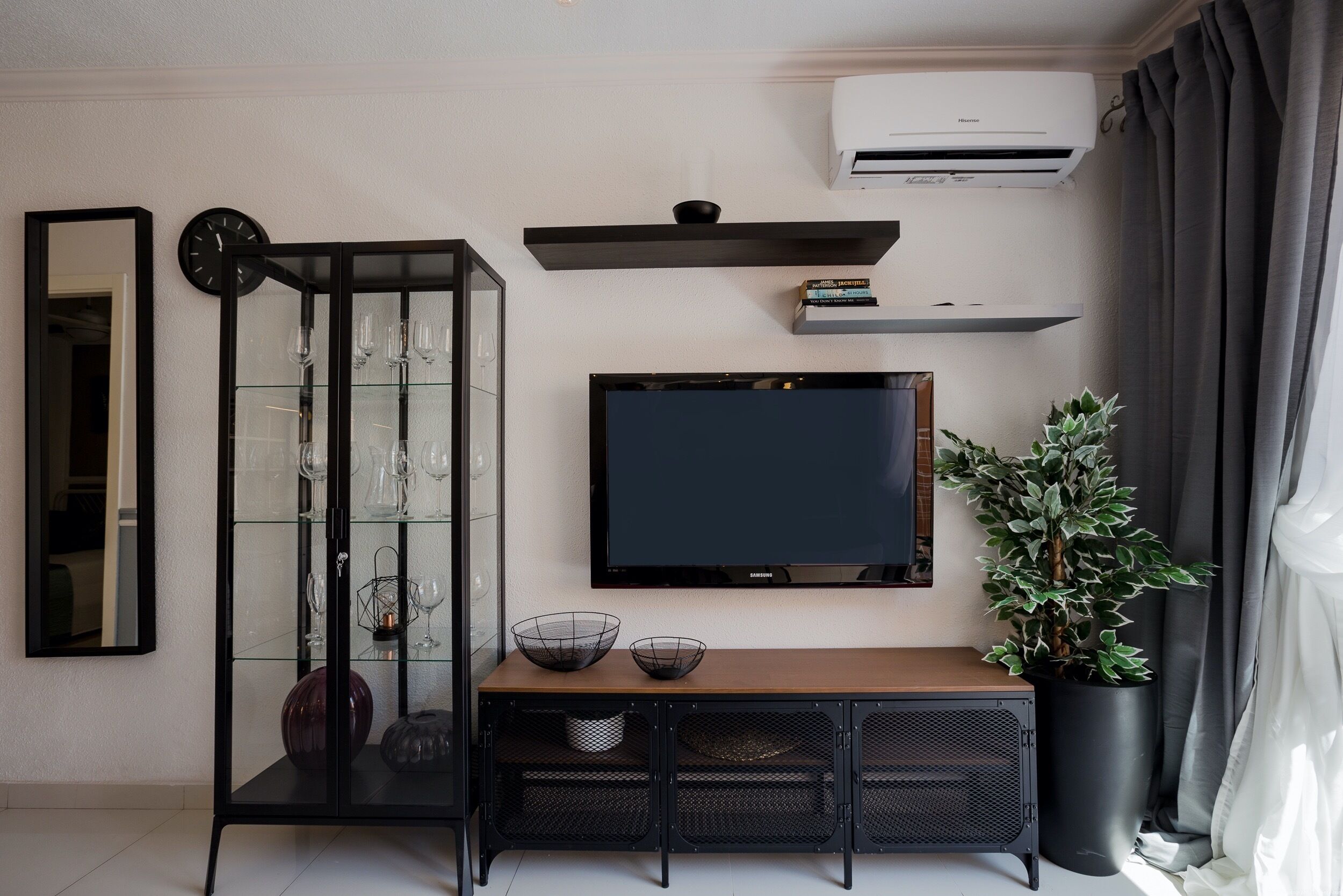 Ein modernes Wohnzimmer mit Flachbildfernseher, einer Glaskabine mit Dekoration, einem Holztischchen und einem Blumentopf.