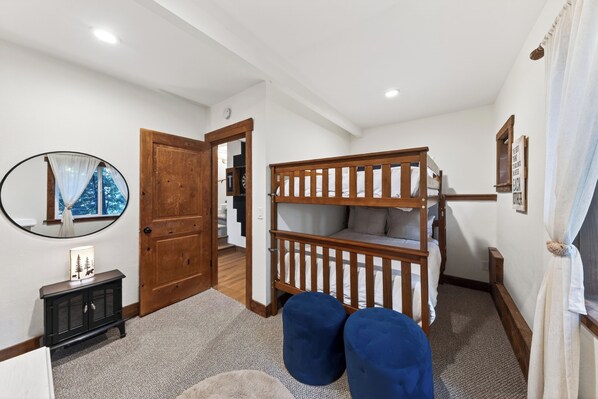 A room with a bunk bed, a small cabinet, a mirror, and a door leading to another room.