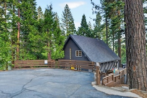 A cabin with a wooden deck, surrounded by tall trees.