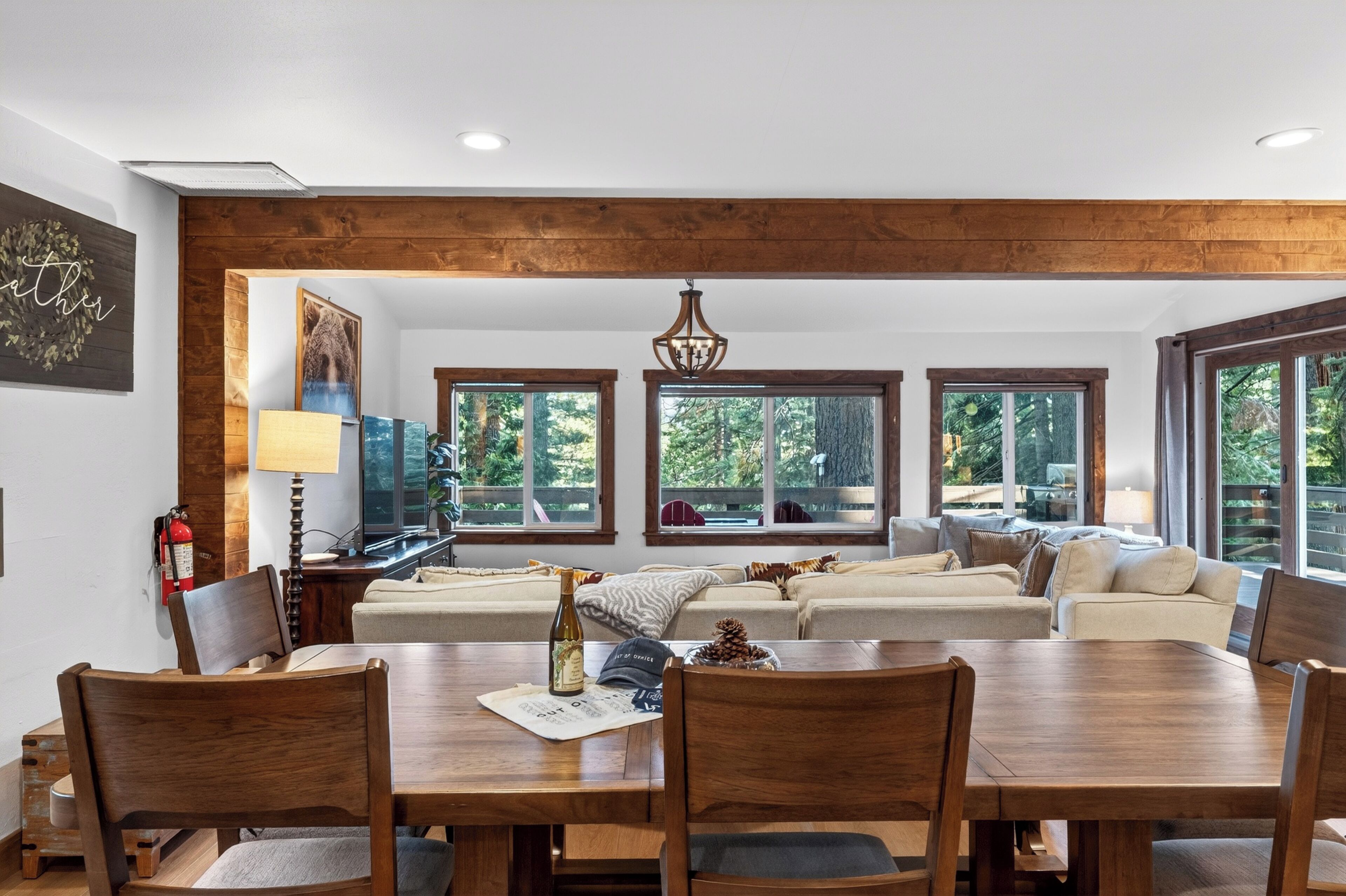 Un salon spacieux avec un plafond en bois, de grandes fenêtres, un coin repas doté d’une table en bois et une cheminée.