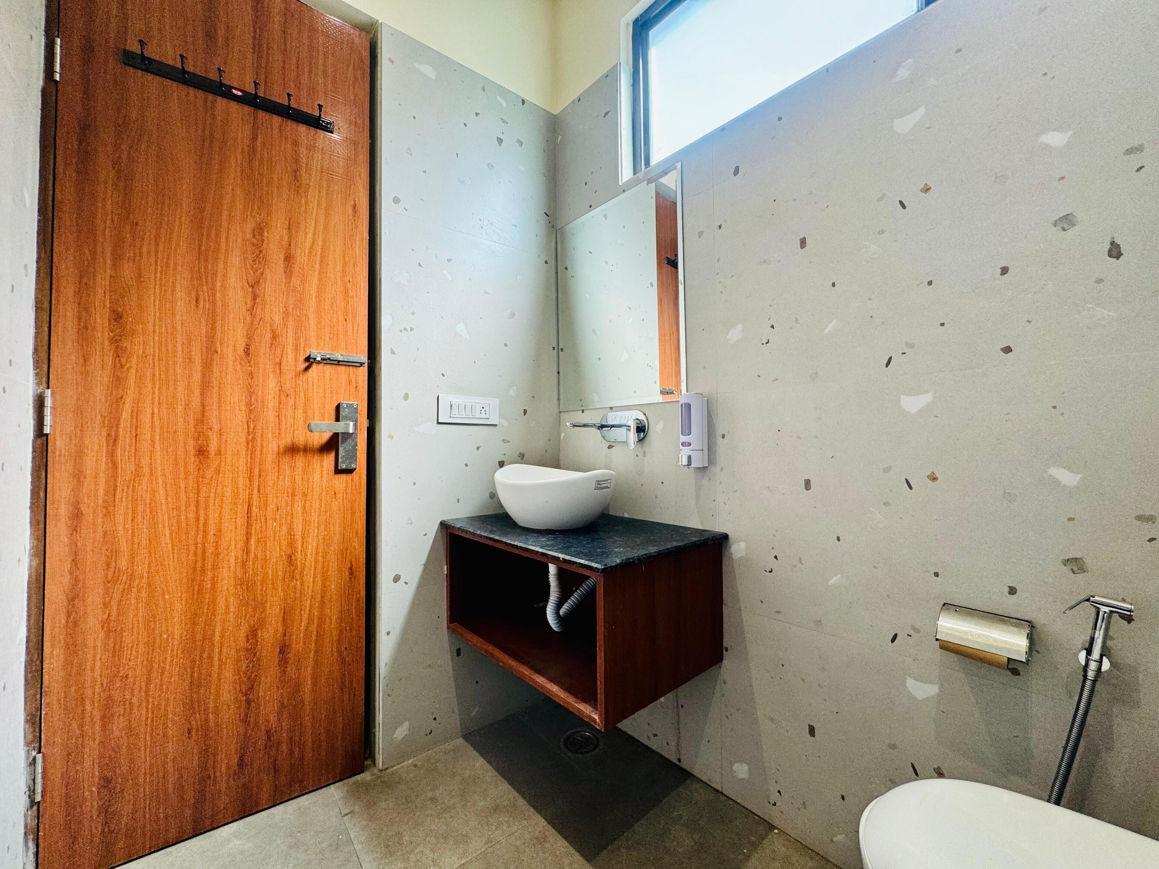 Ein Badezimmer mit Holztür, einem weißen Waschbecken mit Vessel-Becken, einem Spiegel, einem Handtuchspender und einer Toilette.