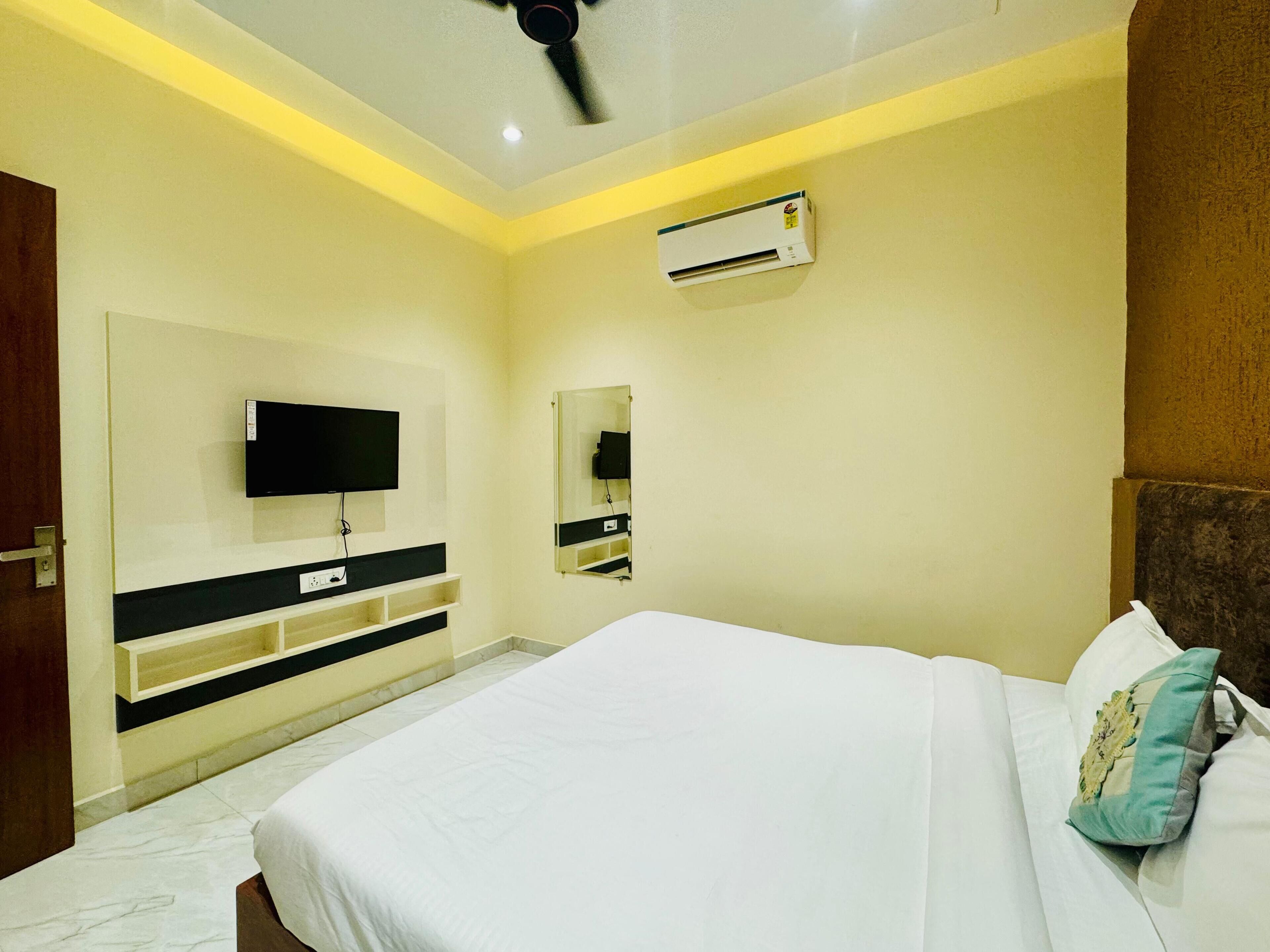 A bedroom with a bed, a TV mounted on the wall, a mirror, and an air conditioning unit.