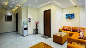 Un moderno vestíbulo de hotel con un sofá, una mesa de centro, dispensador de agua, extintor y un televisor en la pared.