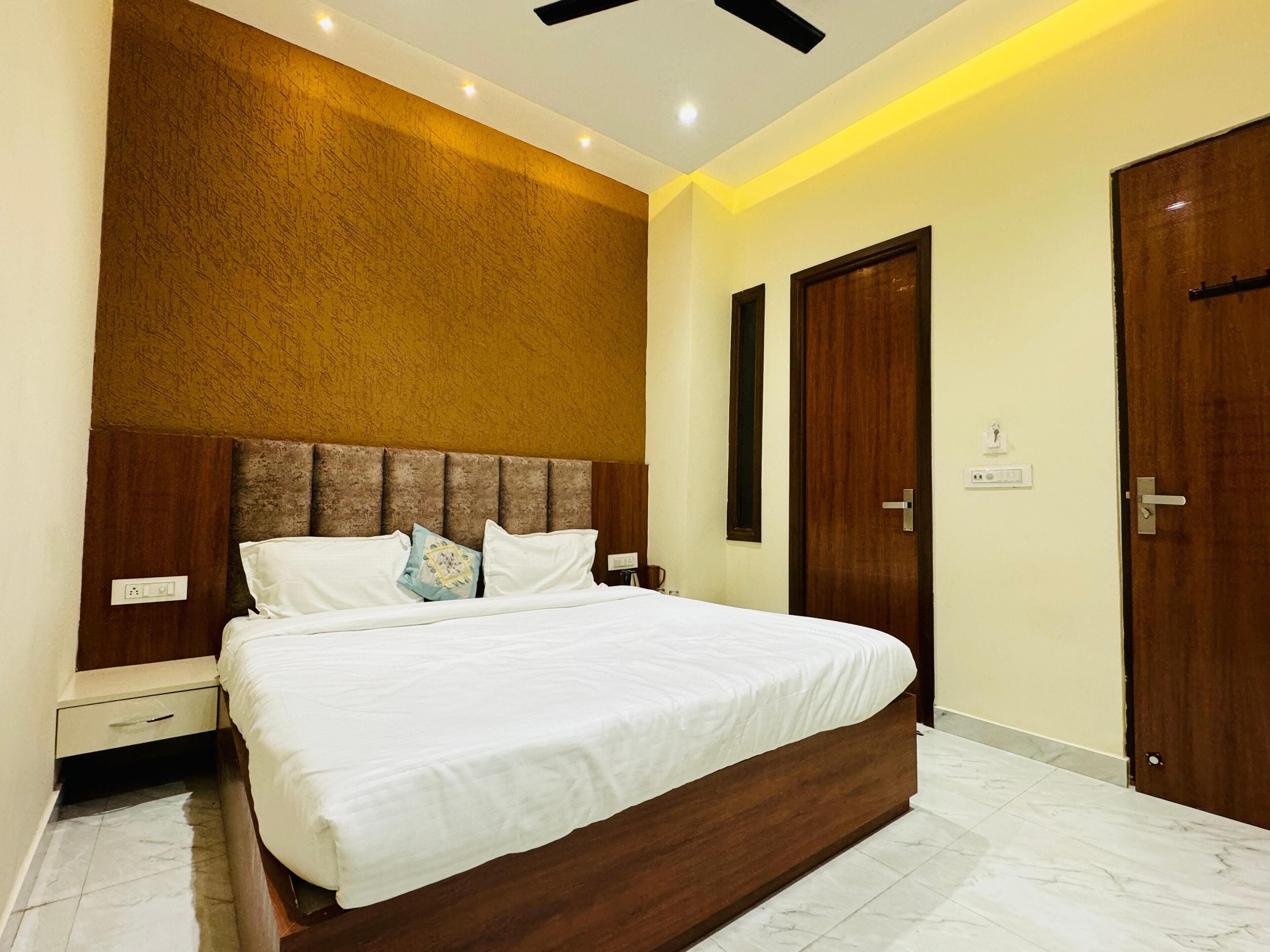 A bedroom with a large bed, a wooden headboard, a wall-mounted light, and two doors.