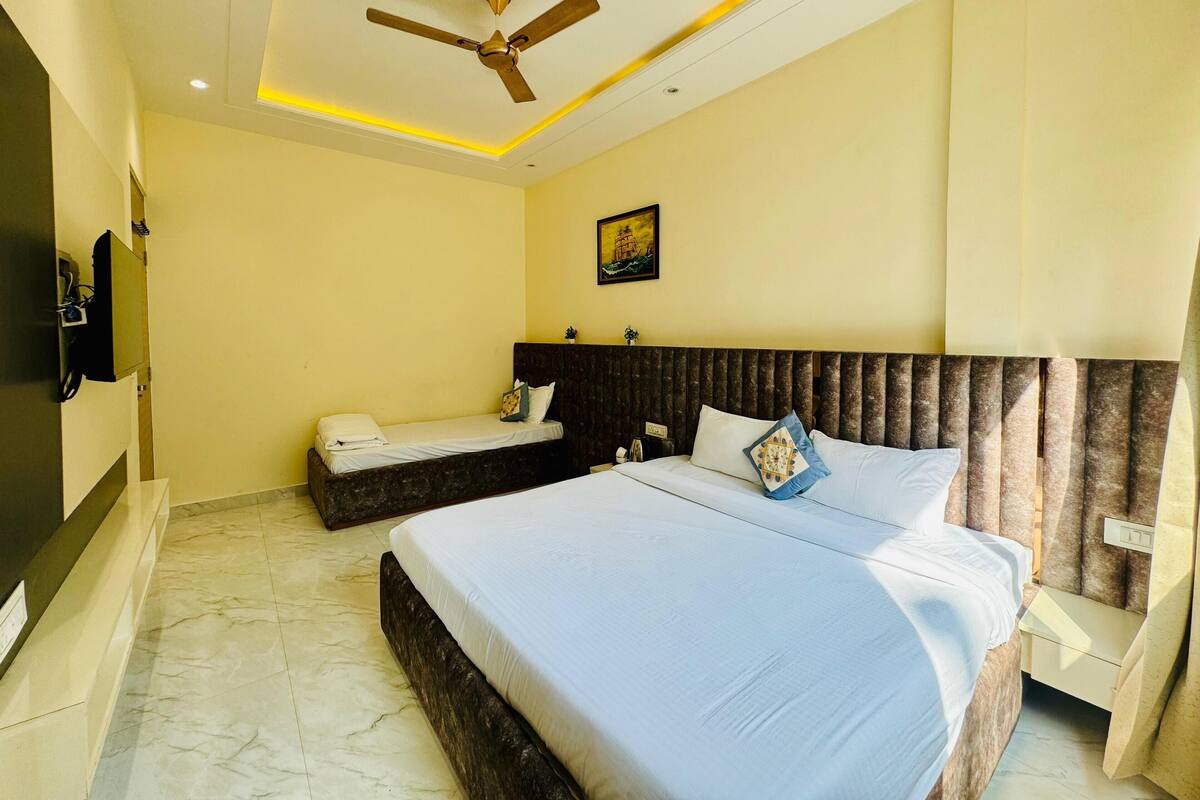 A hotel room with two beds, a ceiling fan, a painting on the wall, and a TV mounted on the wall.