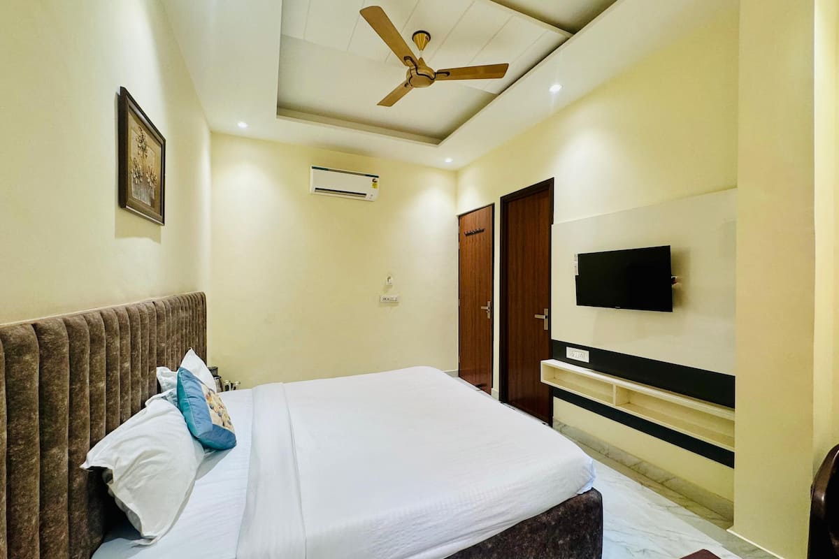 A bedroom with a bed, a ceiling fan, a mounted TV, and an air conditioning unit.