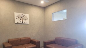 A room with two leather sofas, a wooden coffee table, a wall-mounted painting of a tree with animals, and a small window. - Windale Resorts Munnar (Udumbanchola)