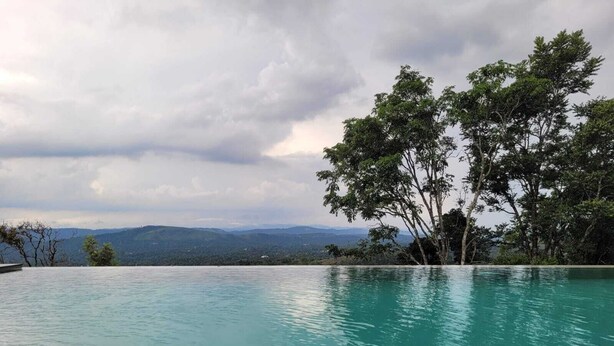 A clear view of a swimming pool with a mountainous landscape in the background. - Windale Resorts Munnar (Udumbanchola)