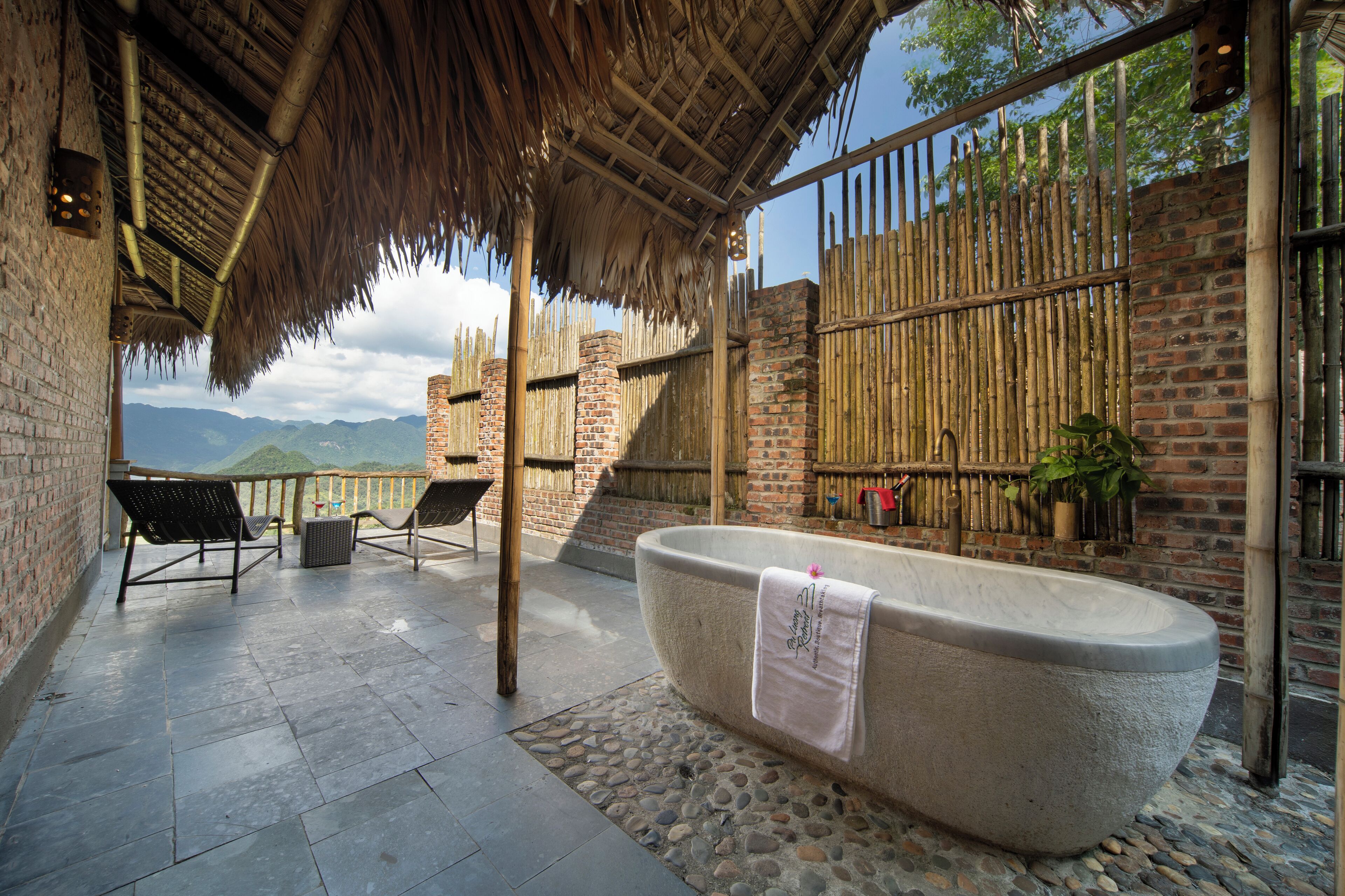 Eine Steinebadewanne mit Handtuch, Sitzgelegenheit im Freien und Blick auf Berge.