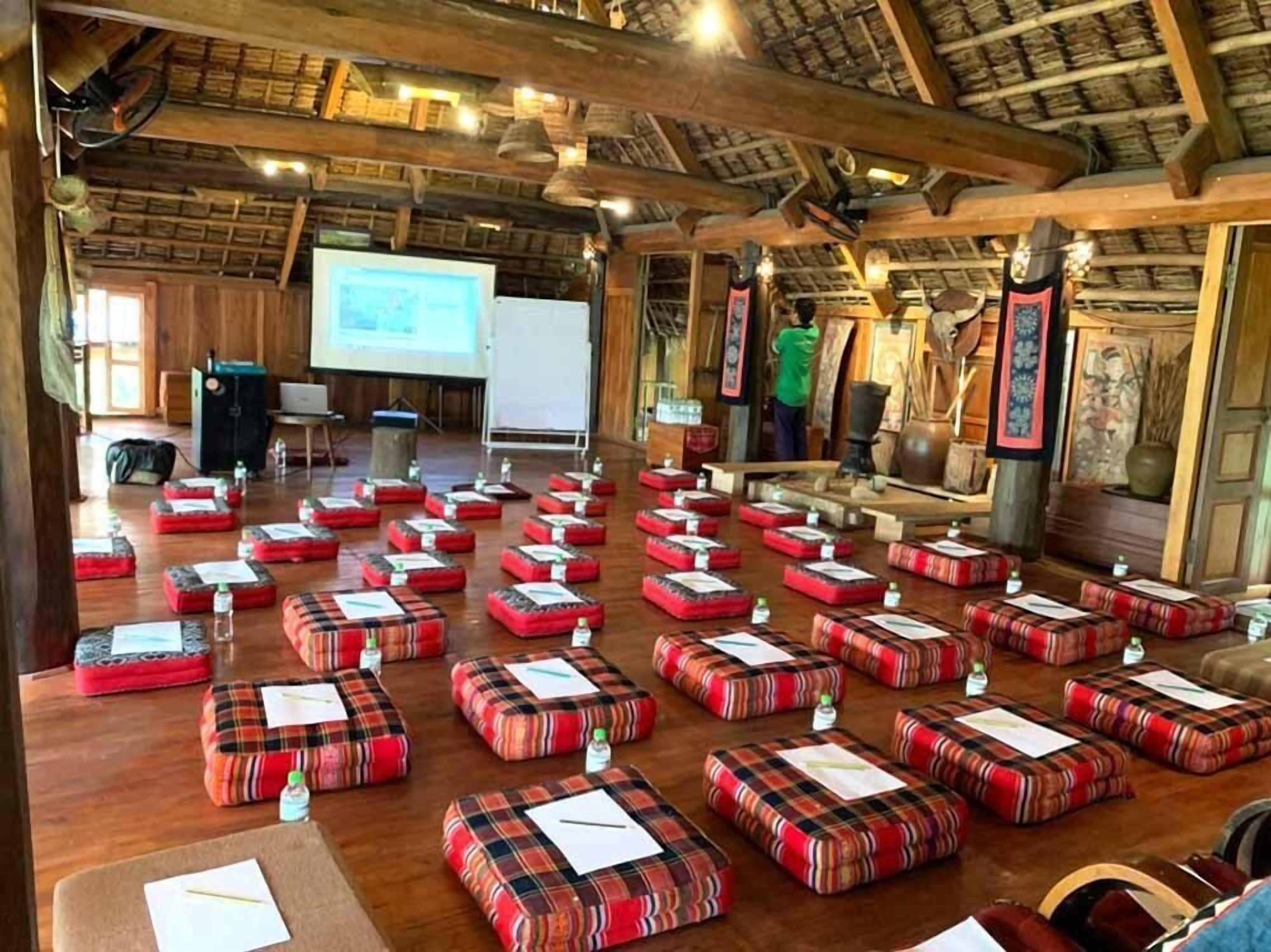A conference room with multiple red and black plaid cushions arranged in rows, a projector screen, and wooden furniture.