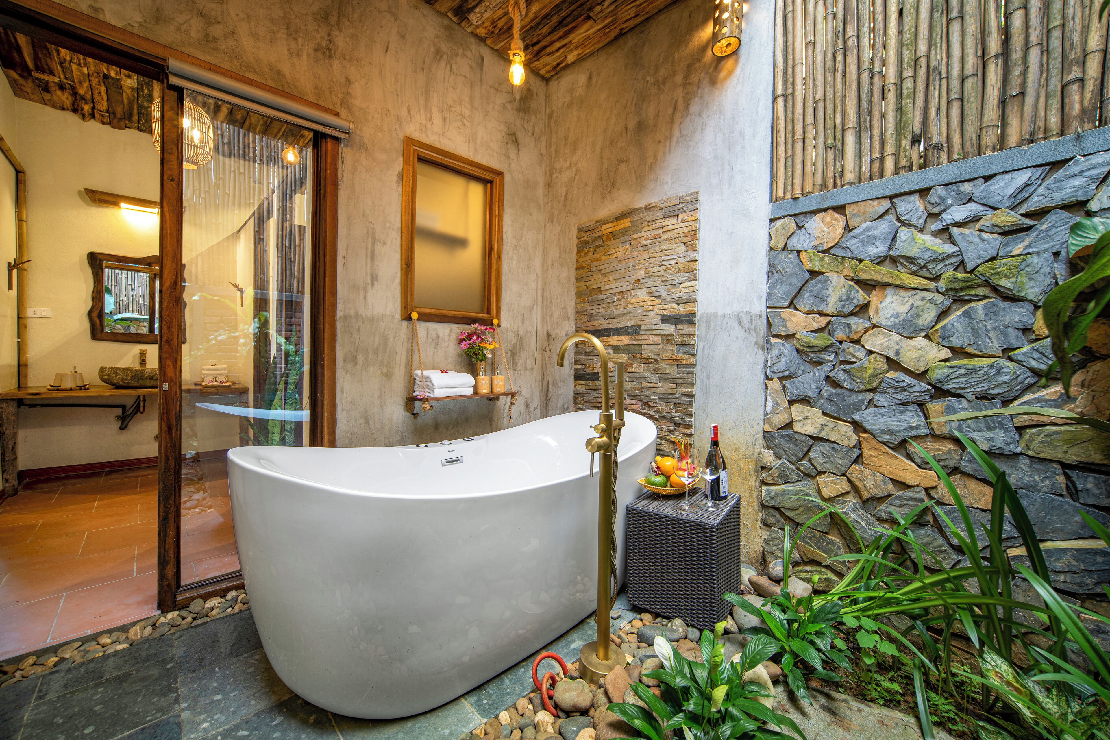 A spacious bathroom with a freestanding bathtub, a stone wall, and a small garden area with plants.