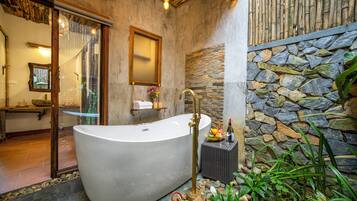 A spacious bathroom with a freestanding bathtub, a stone wall, and a small garden area with plants.