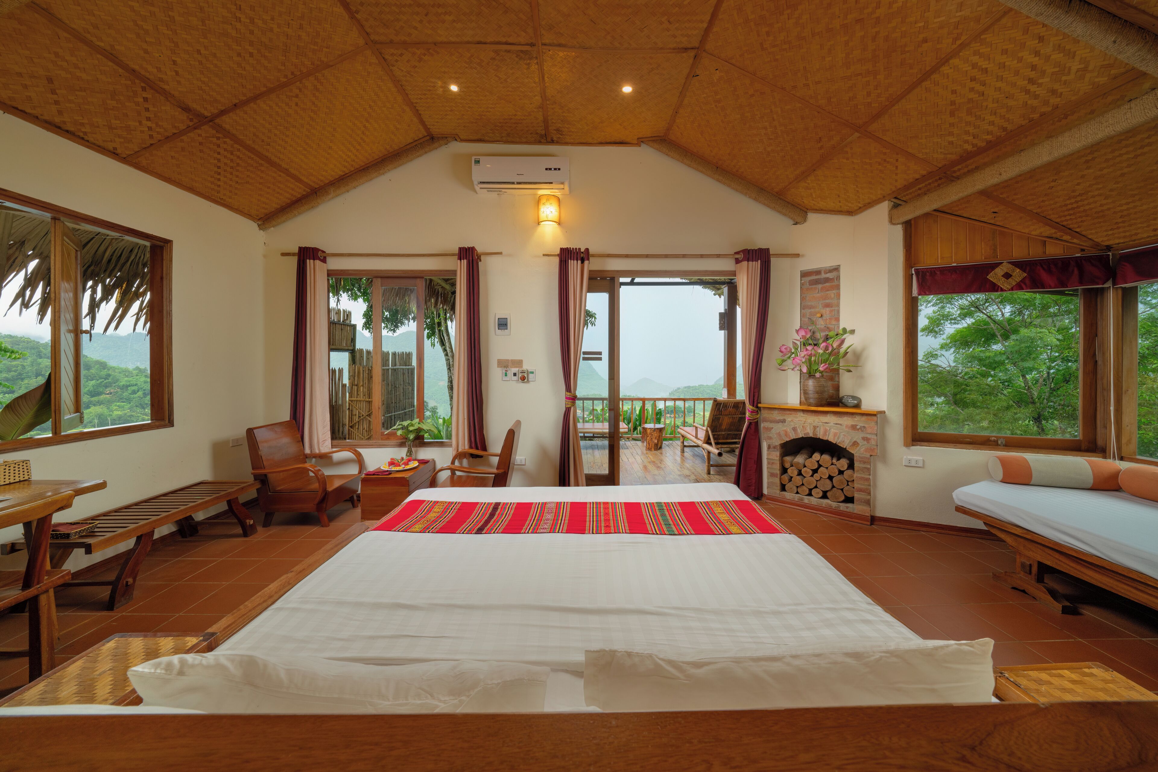 Una habitación amplia con una cama grande, muebles de madera, chimenea y grandes ventanales que ofrecen vistas al exterior.