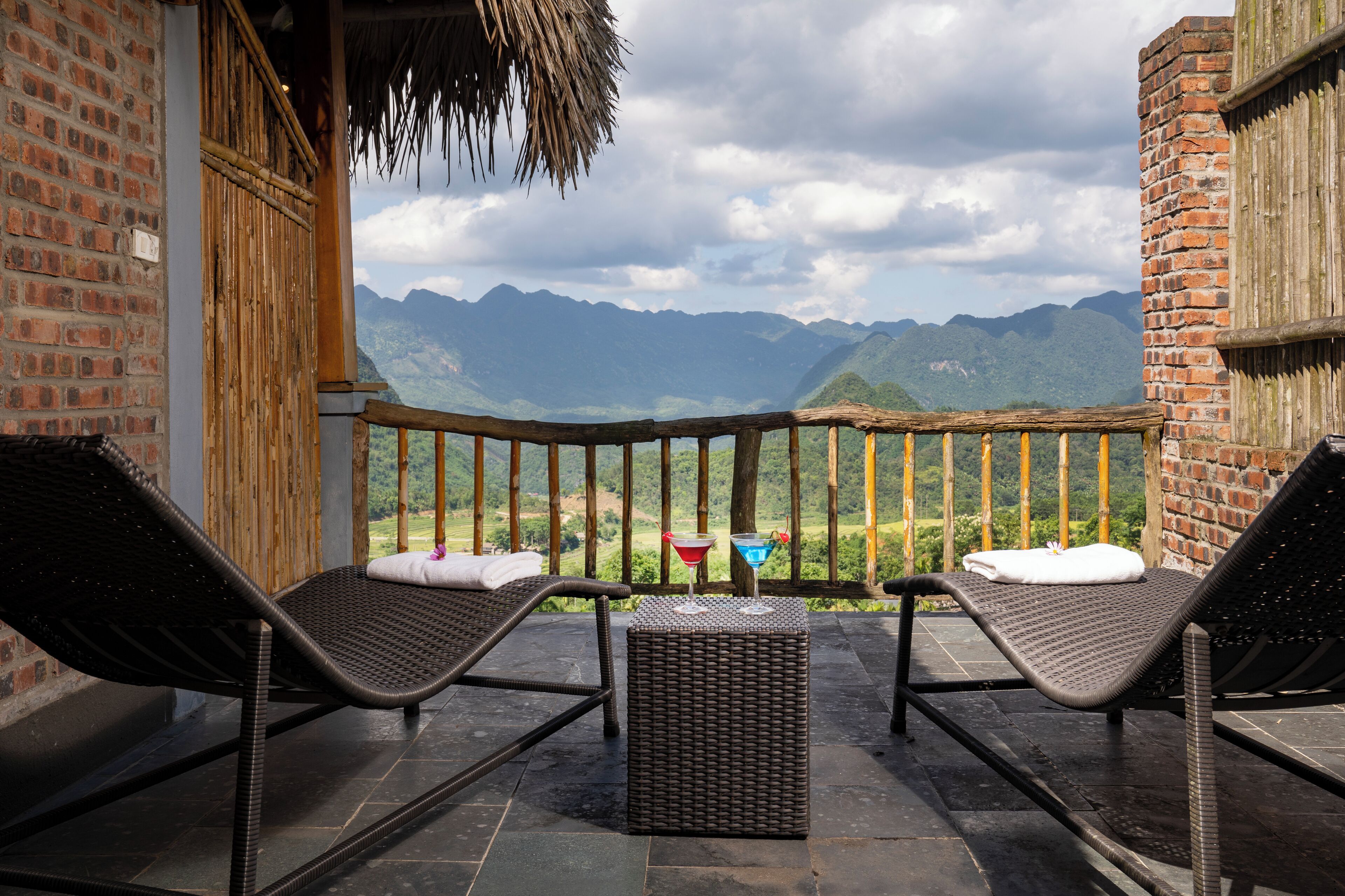 Uma varanda com duas poltronas de vime, uma mesa pequena e vista para as montanhas.