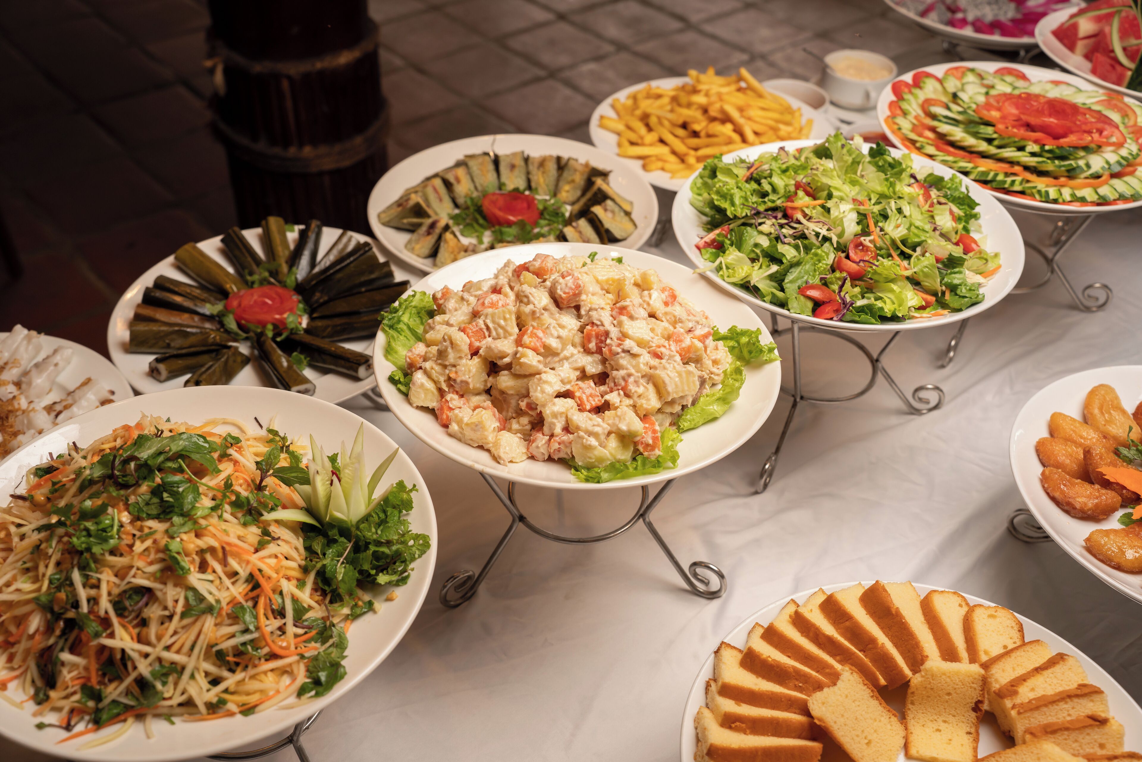 Una variedad de platos en una mesa de buffet, entre ellos ensaladas, sándwiches y otras opciones para picar.