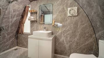 A bathroom with a marble wall, a white sink, a mirror, a shower, and a toilet.